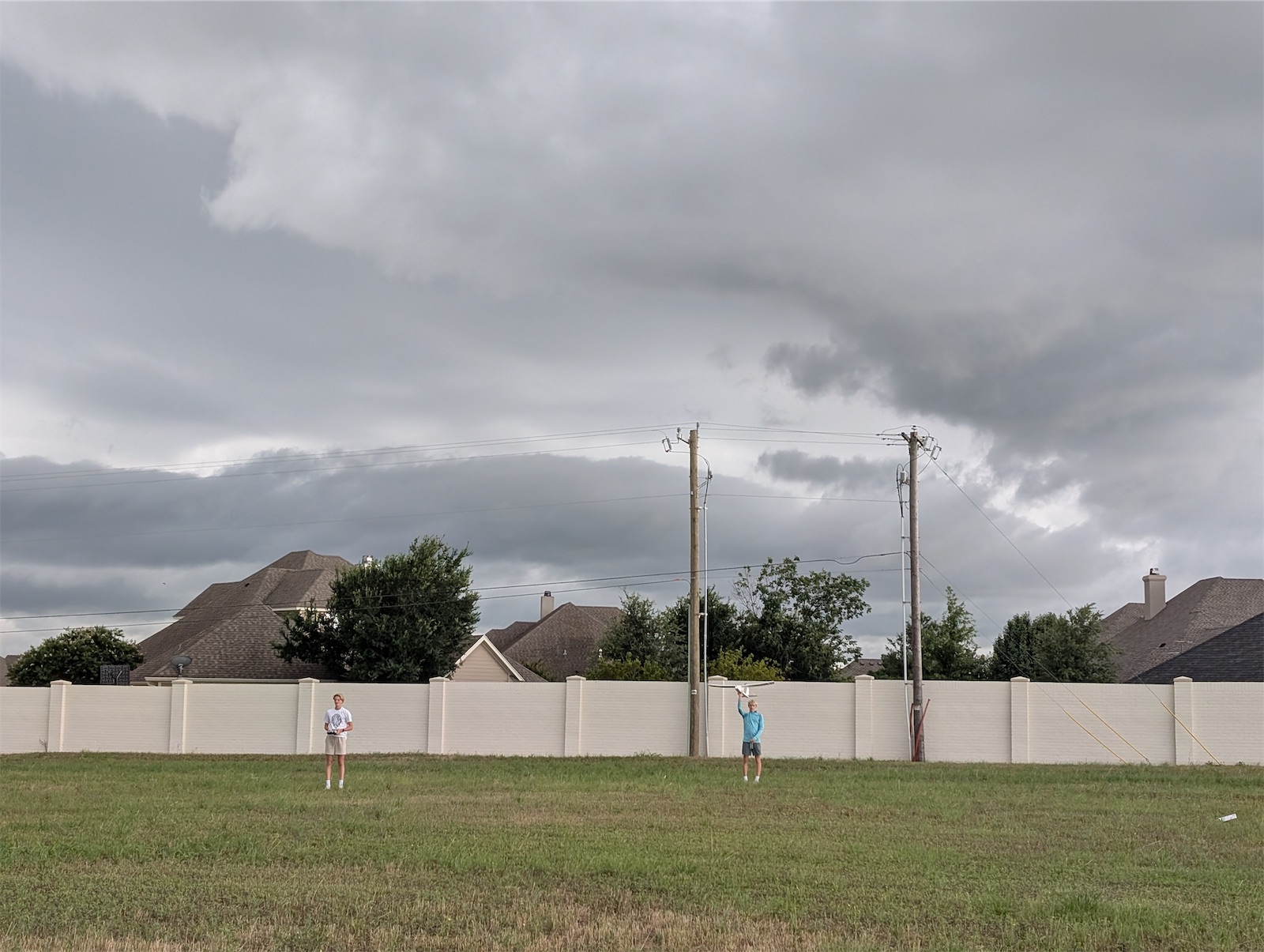 Two members in a field under a stormy sky, one holding the plane up to launch