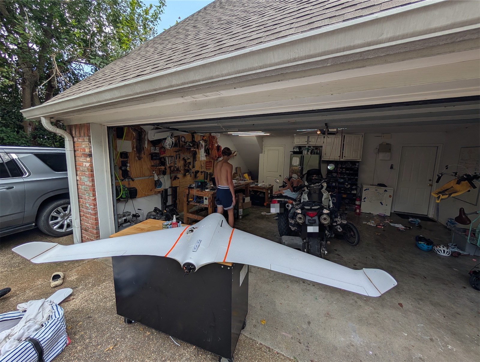 A large white flying-wing aircraft resting on a workbench in front of the garage shop