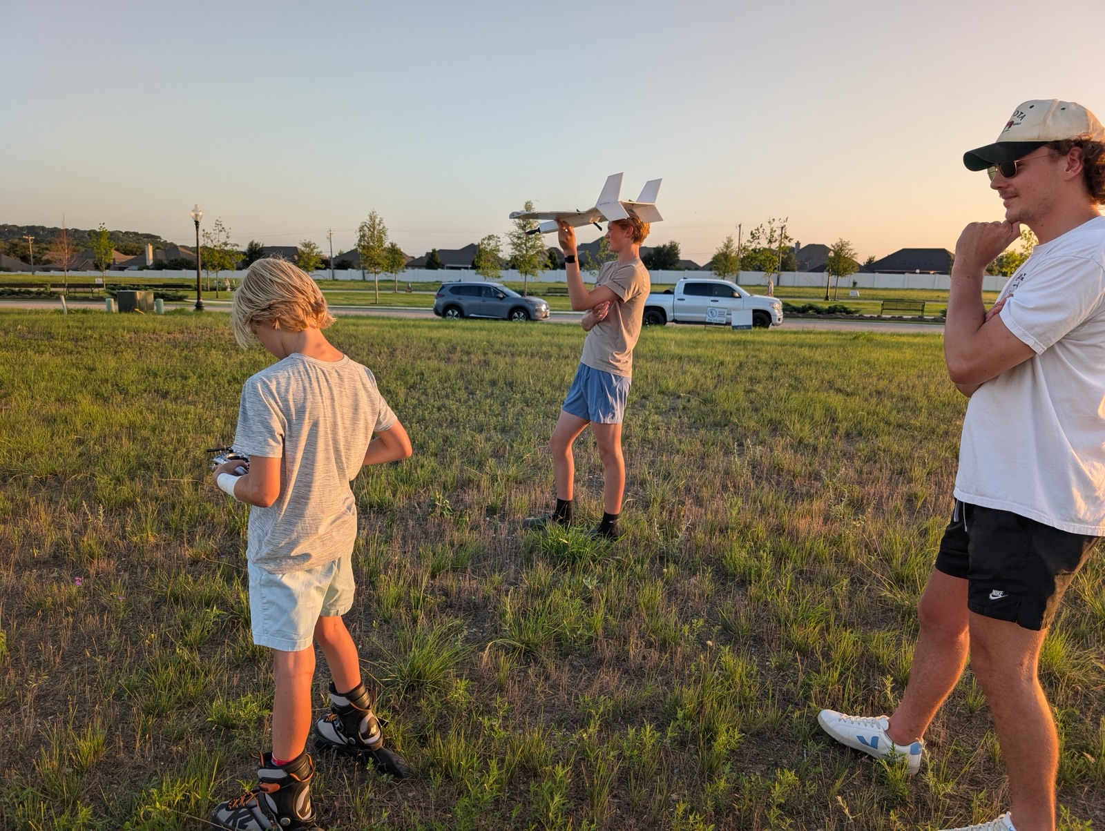 Three members in a field at sunset, one holding the plane overhead while another works the transmitter