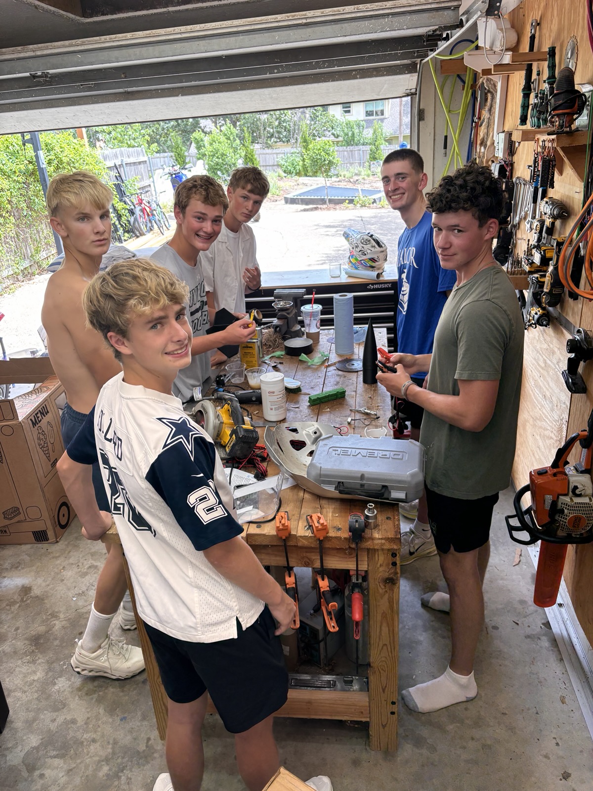 Six club members smiling around the garage workbench during the rocket build