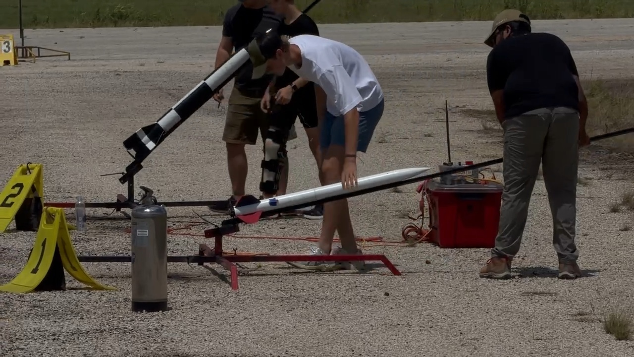 Members and a range volunteer sliding the rocket onto a launch rail lying flat on the pad